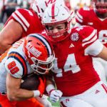 College football defender in red tackles orange-helmet ball carrier during a game.